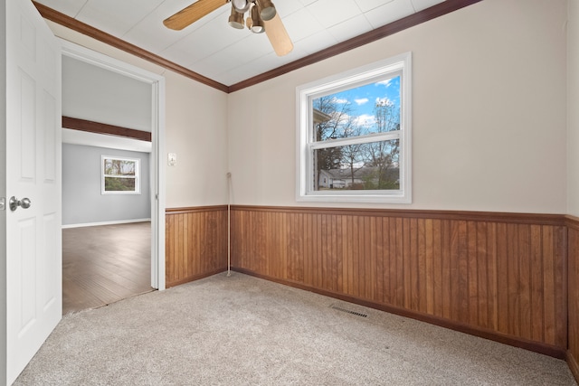 empty room featuring wood walls, ceiling fan, ornamental molding, and light hardwood / wood-style flooring