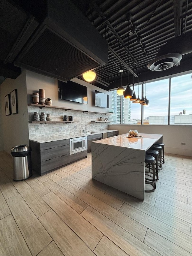 kitchen featuring a breakfast bar, custom exhaust hood, stainless steel microwave, a kitchen island, and light hardwood / wood-style floors