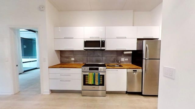 kitchen featuring white cabinets, sink, butcher block counters, and stainless steel appliances