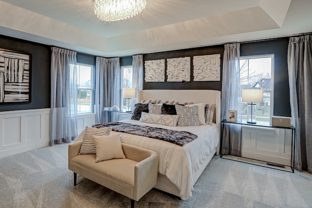 carpeted bedroom with a tray ceiling, multiple windows, and a notable chandelier