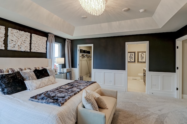 bedroom featuring a spacious closet, connected bathroom, carpet floors, and a tray ceiling