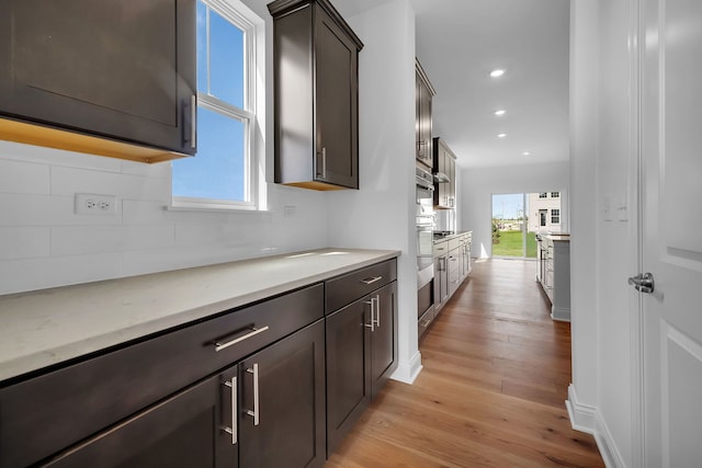 kitchen with dark brown cabinets, light hardwood / wood-style flooring, light stone counters, and tasteful backsplash