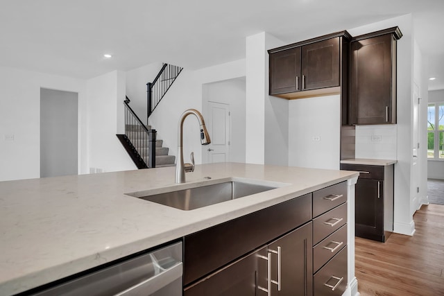 kitchen with light hardwood / wood-style floors, dishwasher, sink, light stone countertops, and dark brown cabinets