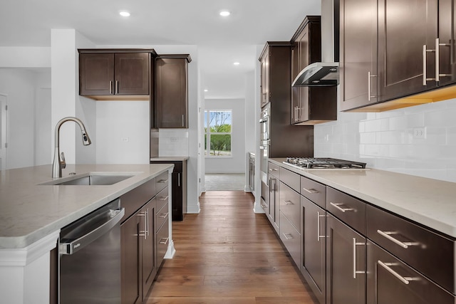 kitchen featuring light stone counters, stainless steel appliances, wall chimney range hood, dark hardwood / wood-style floors, and sink