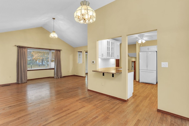 interior space with hanging light fixtures, light hardwood / wood-style flooring, kitchen peninsula, white fridge, and white cabinets