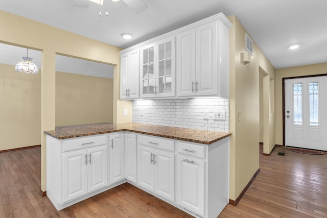 kitchen featuring kitchen peninsula, light wood-type flooring, white cabinetry, and dark stone counters