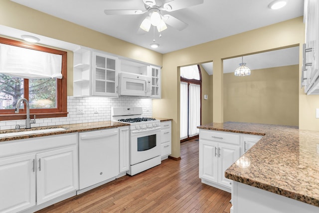 kitchen featuring white appliances, white cabinets, sink, hanging light fixtures, and light wood-type flooring