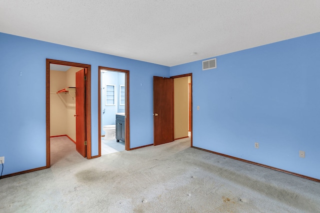 unfurnished bedroom with connected bathroom, a textured ceiling, a walk in closet, light carpet, and a closet