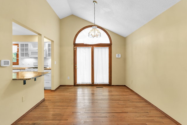 interior space featuring a notable chandelier, light wood-type flooring, a textured ceiling, and high vaulted ceiling