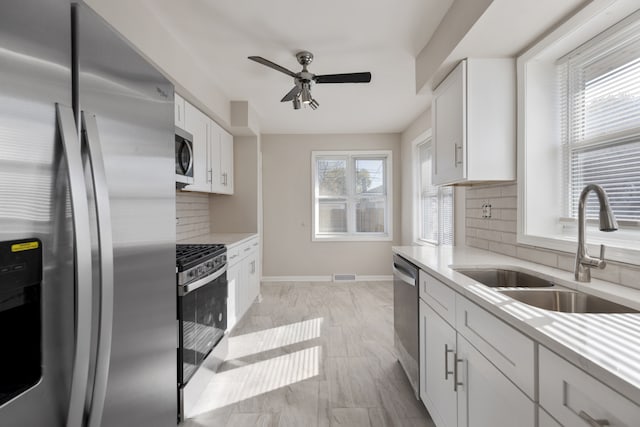 kitchen featuring white cabinets, decorative backsplash, sink, ceiling fan, and appliances with stainless steel finishes