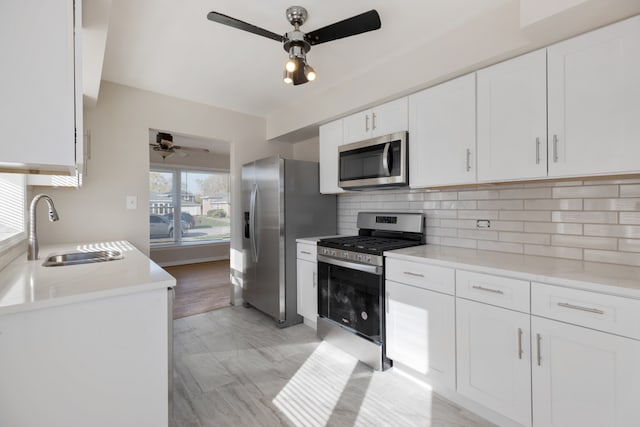 kitchen featuring stainless steel appliances, decorative backsplash, sink, white cabinets, and ceiling fan