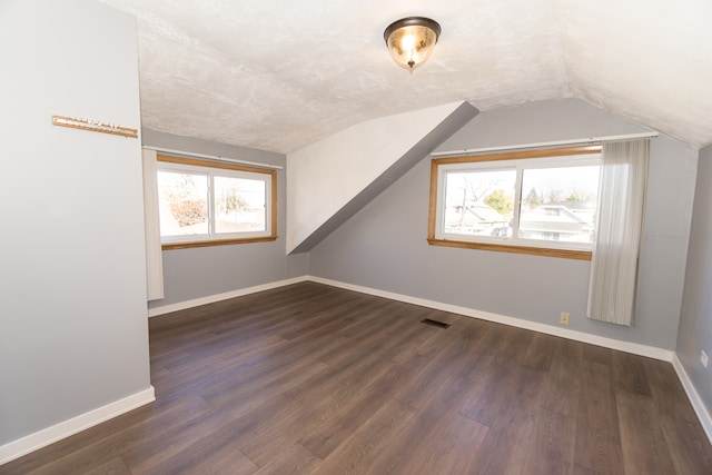 additional living space featuring dark wood-type flooring, a wealth of natural light, and vaulted ceiling