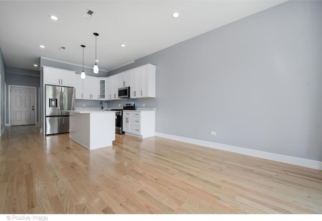 kitchen with stainless steel appliances, white cabinets, hanging light fixtures, a kitchen island, and light hardwood / wood-style flooring