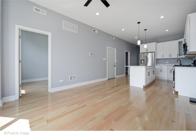 kitchen featuring light hardwood / wood-style floors, white cabinetry, hanging light fixtures, a center island, and stainless steel fridge