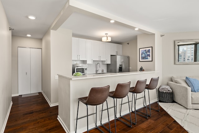 kitchen featuring appliances with stainless steel finishes, dark hardwood / wood-style flooring, a kitchen breakfast bar, white cabinets, and kitchen peninsula