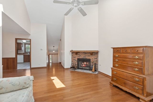 living room with a fireplace, light hardwood / wood-style floors, ceiling fan, and a towering ceiling