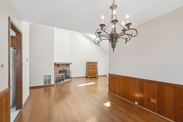 unfurnished living room with a chandelier, wooden walls, light hardwood / wood-style floors, and a brick fireplace