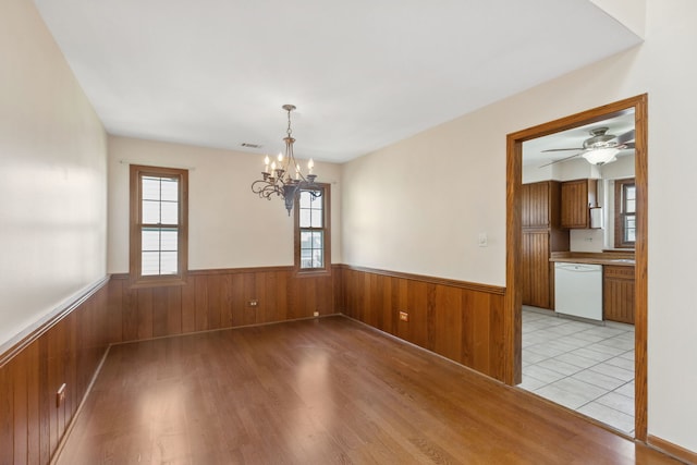 spare room featuring wood walls, light wood-type flooring, and ceiling fan with notable chandelier