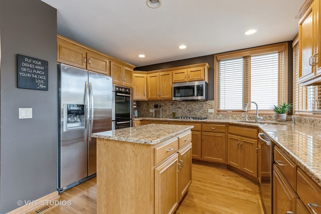 kitchen with a center island, backsplash, appliances with stainless steel finishes, light hardwood / wood-style floors, and light stone counters