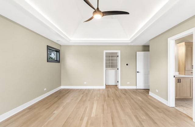 unfurnished bedroom featuring ceiling fan, light hardwood / wood-style flooring, a spacious closet, and a tray ceiling