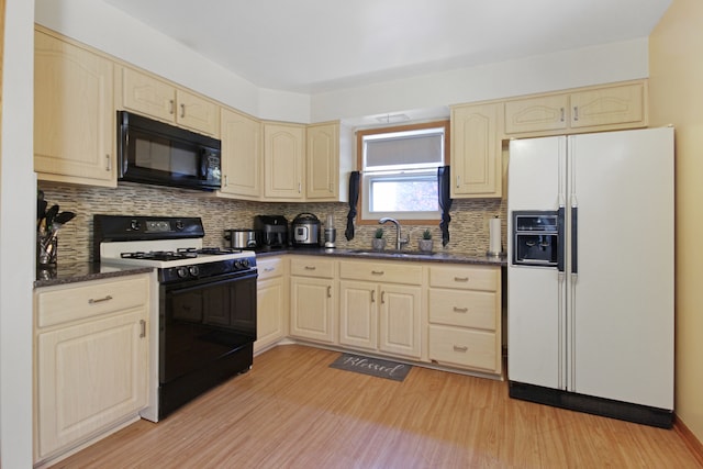 kitchen featuring black appliances, tasteful backsplash, light wood-type flooring, sink, and dark stone countertops