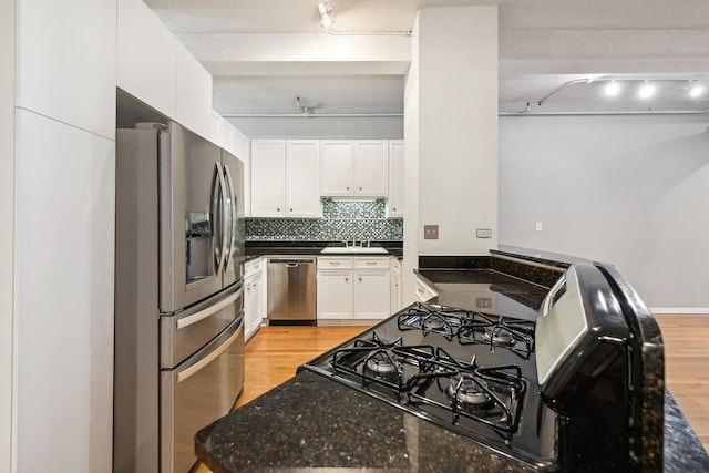 kitchen with appliances with stainless steel finishes, backsplash, dark stone counters, light hardwood / wood-style flooring, and white cabinets