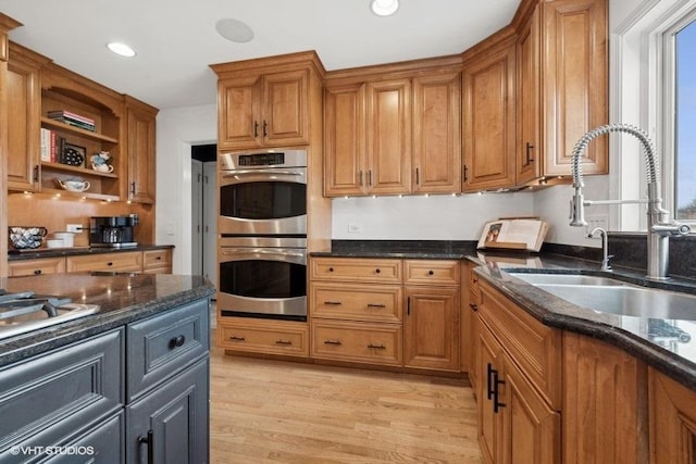 kitchen with double oven, dark stone counters, sink, and light hardwood / wood-style flooring