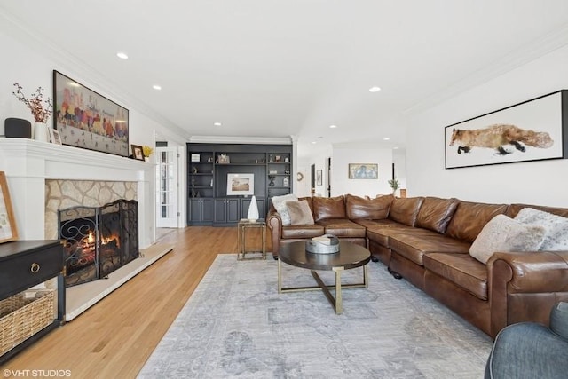 living room featuring hardwood / wood-style floors, built in shelves, crown molding, and a fireplace