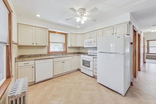 kitchen featuring sink, radiator heating unit, white appliances, ceiling fan, and light stone counters