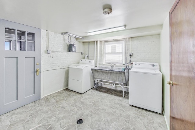 laundry room featuring washing machine and dryer, sink, and brick wall