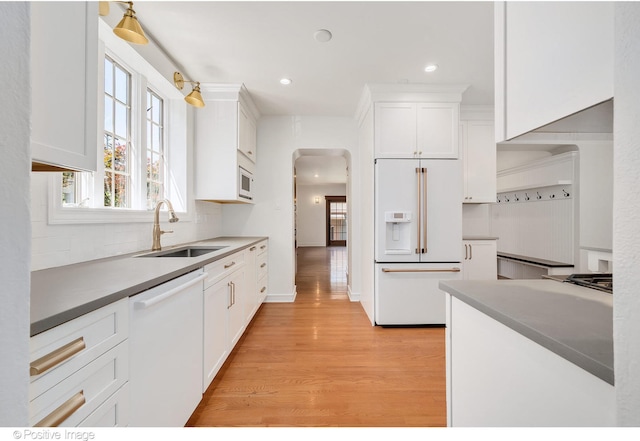 kitchen with white cabinetry, decorative backsplash, sink, white appliances, and light hardwood / wood-style flooring