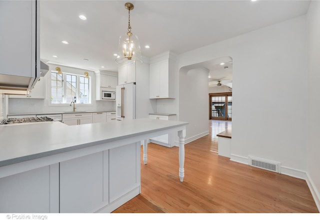 kitchen with white cabinetry, ceiling fan with notable chandelier, hanging light fixtures, white appliances, and light wood-type flooring