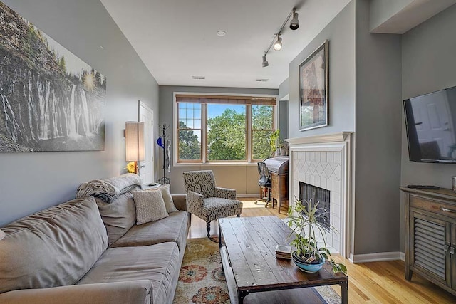 living room with a tile fireplace, rail lighting, and light hardwood / wood-style flooring