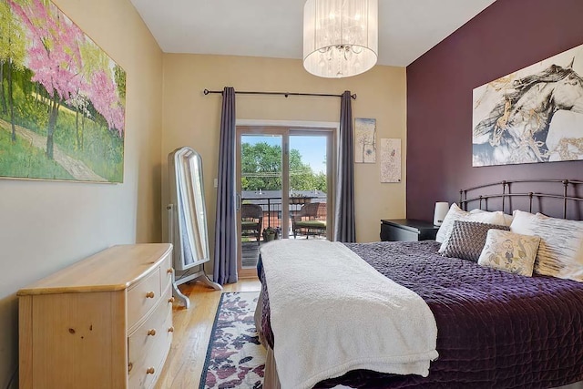 bedroom with access to exterior, an inviting chandelier, and light hardwood / wood-style flooring