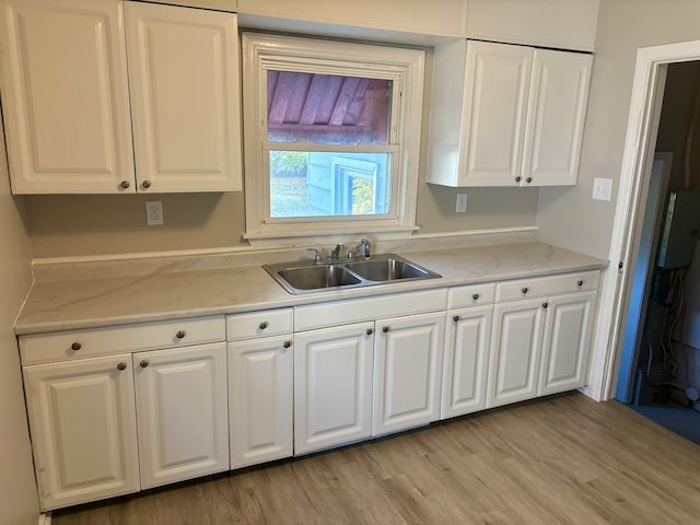 kitchen with light wood-type flooring, sink, light stone counters, and white cabinets