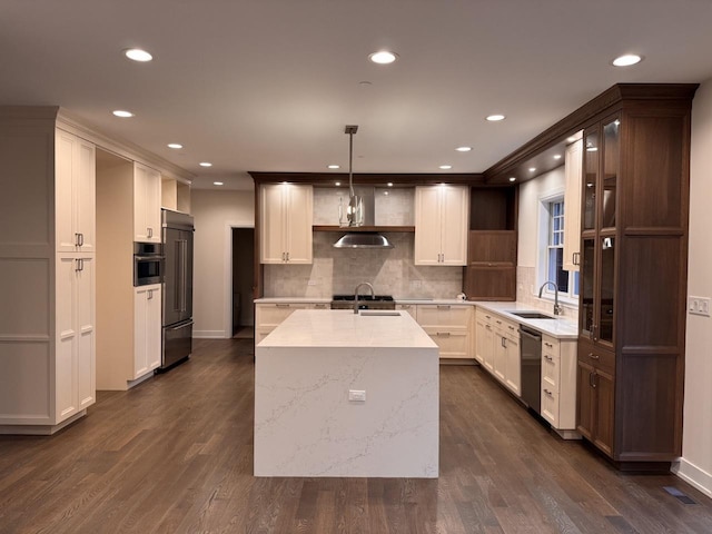 kitchen with a center island with sink, sink, hanging light fixtures, dark hardwood / wood-style floors, and appliances with stainless steel finishes