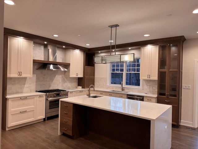 kitchen with wall chimney range hood, hanging light fixtures, dark hardwood / wood-style floors, an island with sink, and stainless steel appliances