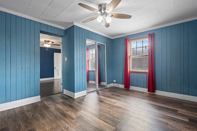 empty room featuring crown molding, wooden walls, ceiling fan, and dark wood-type flooring