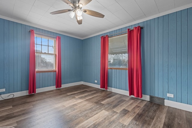 empty room featuring dark hardwood / wood-style floors, ceiling fan, crown molding, and wood walls