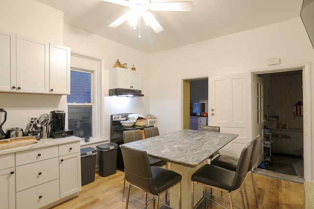 kitchen featuring ceiling fan, a kitchen island, light hardwood / wood-style flooring, a breakfast bar area, and white cabinets