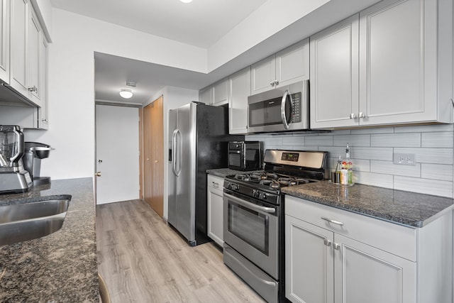 kitchen featuring dark stone counters, white cabinetry, light hardwood / wood-style flooring, and stainless steel appliances