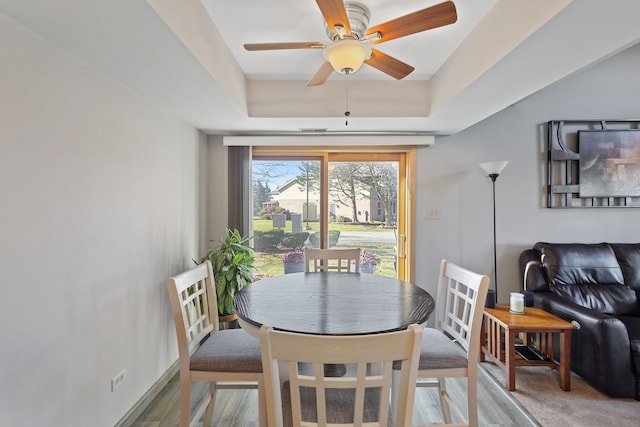 dining space featuring hardwood / wood-style flooring, ceiling fan, and a raised ceiling