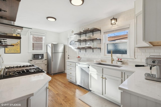 kitchen with light stone counters, a sink, white cabinets, appliances with stainless steel finishes, and open shelves