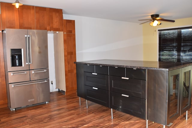 kitchen with high end refrigerator, ceiling fan, dark stone counters, and wood-type flooring