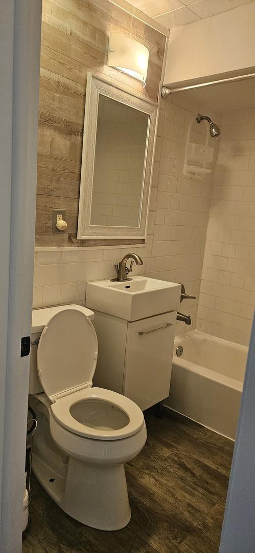 full bathroom featuring vanity, wood-type flooring, tile walls, toilet, and tiled shower / bath