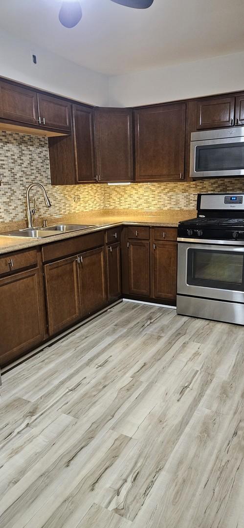 kitchen with appliances with stainless steel finishes, tasteful backsplash, light hardwood / wood-style flooring, and sink