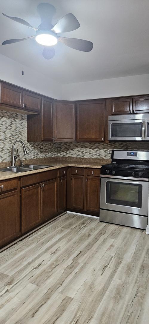 kitchen with tasteful backsplash, sink, light hardwood / wood-style flooring, and appliances with stainless steel finishes