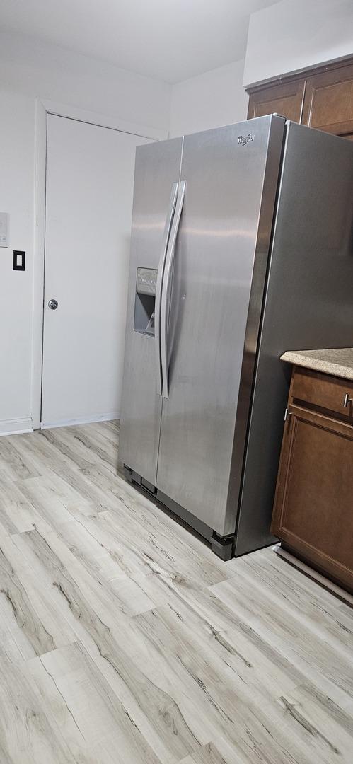 kitchen with stainless steel refrigerator with ice dispenser, light wood-type flooring, and dark brown cabinets