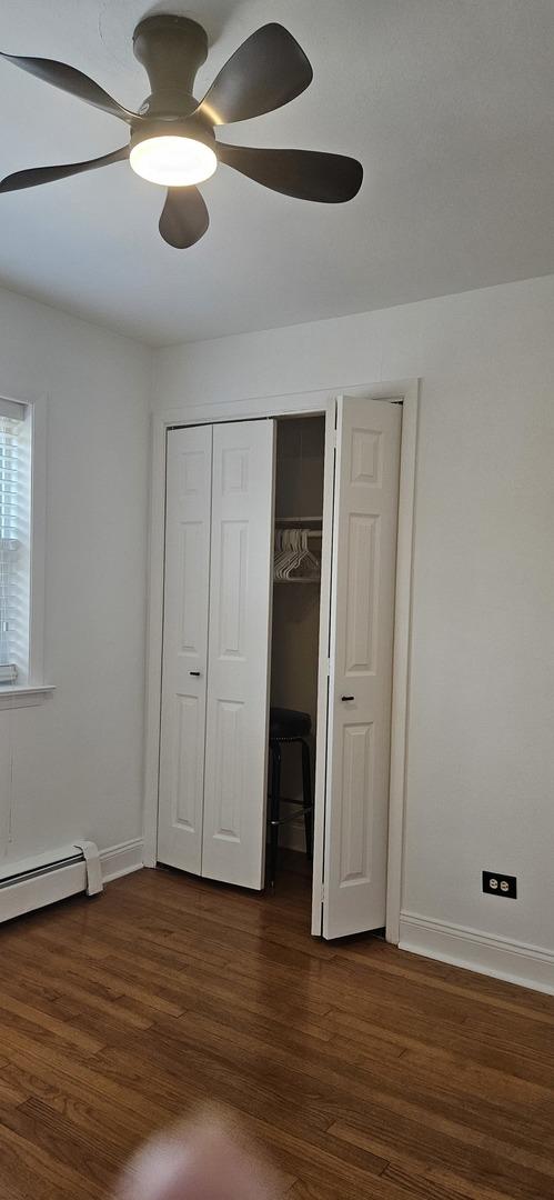 unfurnished bedroom featuring dark hardwood / wood-style flooring, ceiling fan, and a baseboard heating unit