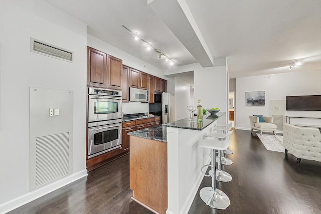 kitchen featuring appliances with stainless steel finishes, dark hardwood / wood-style floors, a breakfast bar area, and dark stone countertops